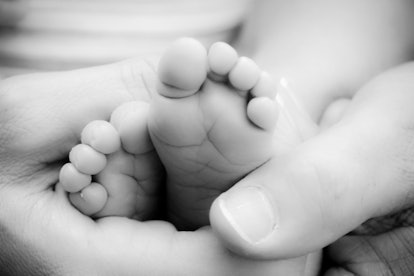 A close-up of a parent's hand holding a newborn's foot
