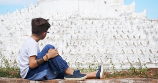 An autistic boy sitting on the ground and looking at a white building with wave-like ornaments