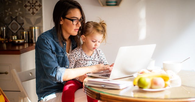 A working mom on her laptop while holding her daughter on her lap in a kitchen