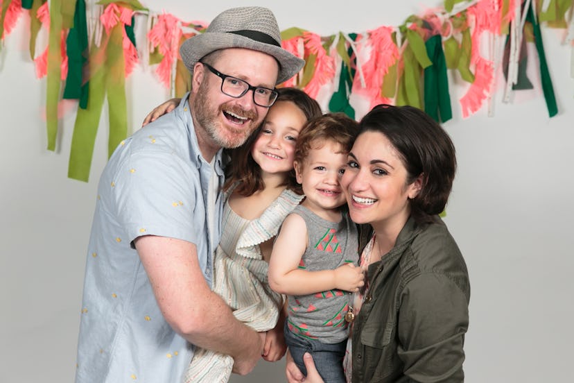 A dad and working mom posing for a photo while holding their son and daughter during a party