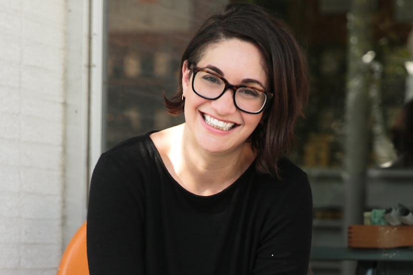 A working mom smiling with a short black bob wearing a black sweater and black glasses