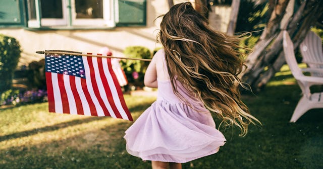 A long-haired brunette girl in a lilac dress twisting and turning in place while holding an American...