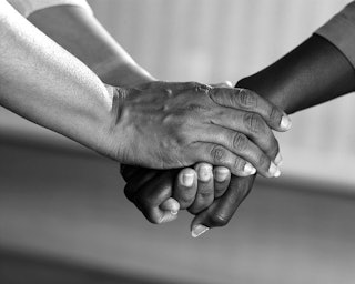 A close-up of two pairs of hands holding each other in a supporting manner in black and white