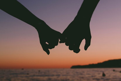Two people holding hands by the pinky finger with a sunset in the background