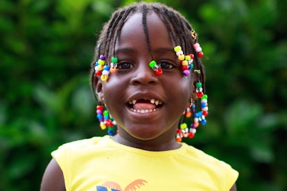 A young girl in a yellow shirt with braids is smiling.