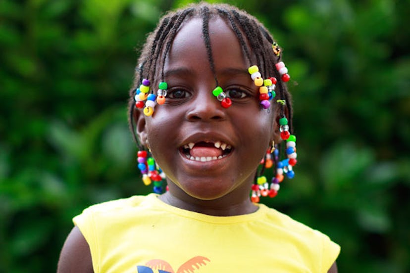 A young girl in a yellow shirt with braids is smiling.