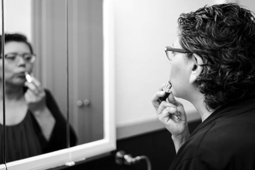 Woman putting her lipstick on in the bathroom and noticing rogue chin hairs