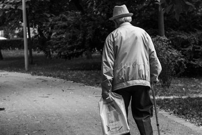 An old man with a cane and a bag walking alone in the park