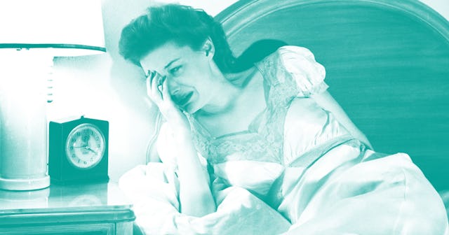 An exhausted mother crying in bed while leaning on the pillow with a clock on her nightstand showing...
