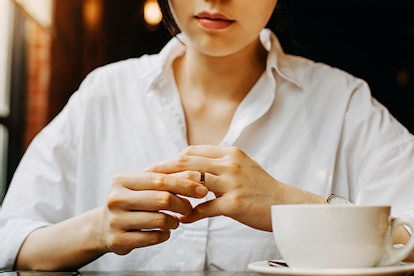 A woman in a white shirt having a cup of coffee and removing her ring because of having an affair