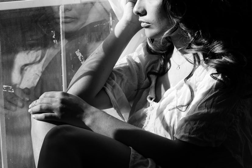 A worried and sad woman sitting next to a window and looking through it in black and white