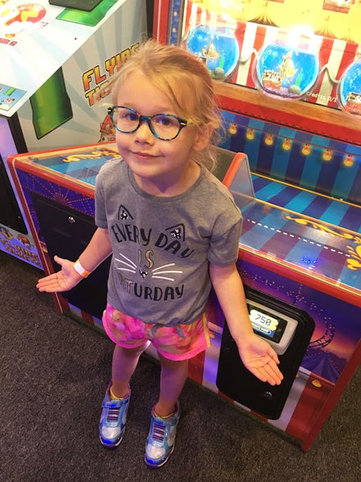 A small girl standing in front of a game machine at an arcade