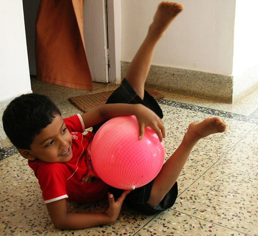 A small boy plays on the floor with a pink balloon