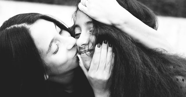 A mother kissing her teen daughter on the cheek in black and white