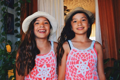 Two girl twins wearing hats and orange-white dresses smiling