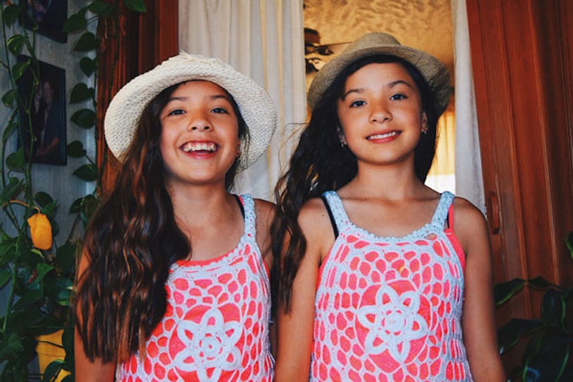 Two girl twins wearing hats and orange-white dresses smiling