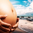A mother in the second trimester holding her pregnant belly with the beach and sea in the background...