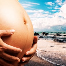 A mother in the second trimester holding her pregnant belly with the beach and sea in the background...