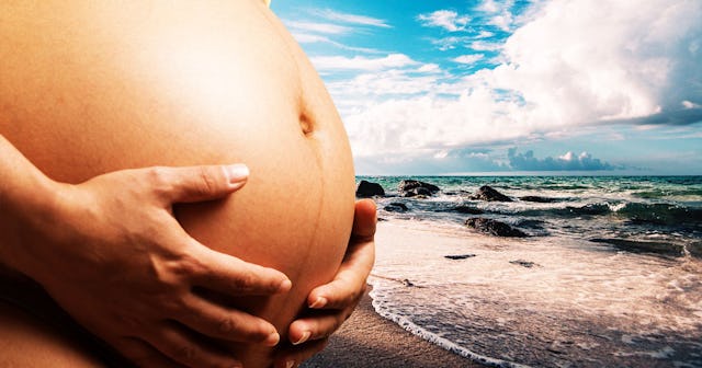 A mother in the second trimester holding her pregnant belly with the beach and sea in the background...