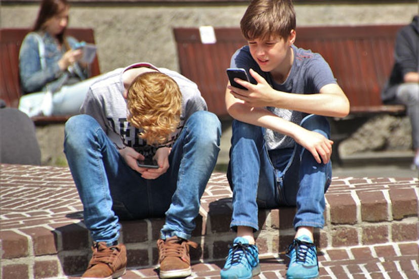 Two teen boys sitting on the ground while looking at their phones 