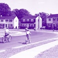 Two children riding their bikes down a street with rows of houses on both sides, all blue-toned blac...