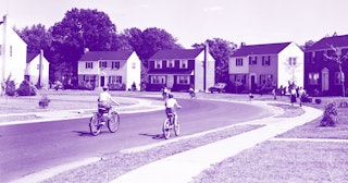 Two children riding their bikes down a street with rows of houses on both sides, all blue-toned blac...