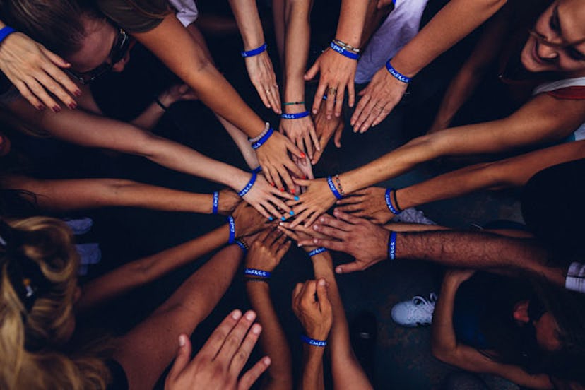 A group of girls reaching their hands in a huddle, supporting each other with blue and white armband...