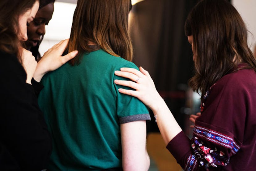 A girl in a green T-shirt from her back being comforted by three other women leaning their hands on ...