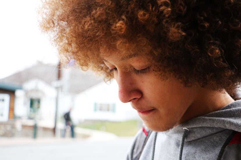 A close-up of a curly-haired tween in a grey hoodie looking down in the middle of a street