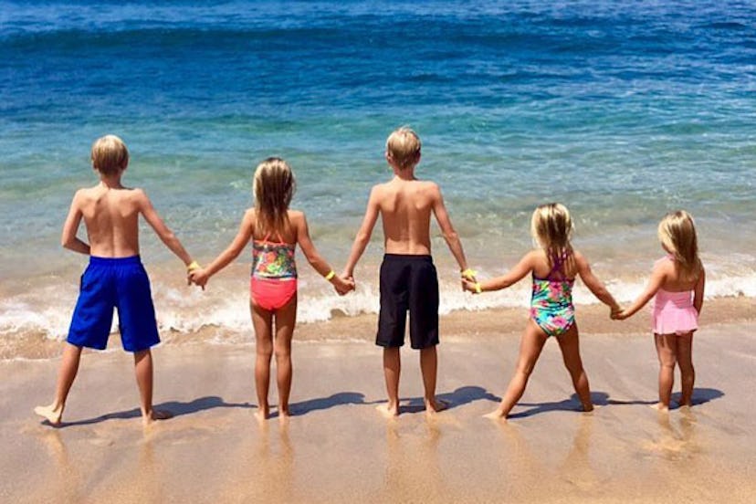 Tara Schoeller's children holding their hands at a sand beach next to the sea