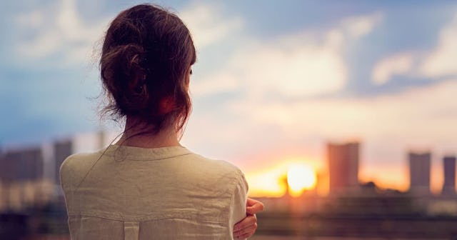 A woman in a white shirt looking at the city view while thinking about her miscarriage