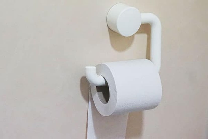 A roll of toilet paper on a white hanger attached to a white wall