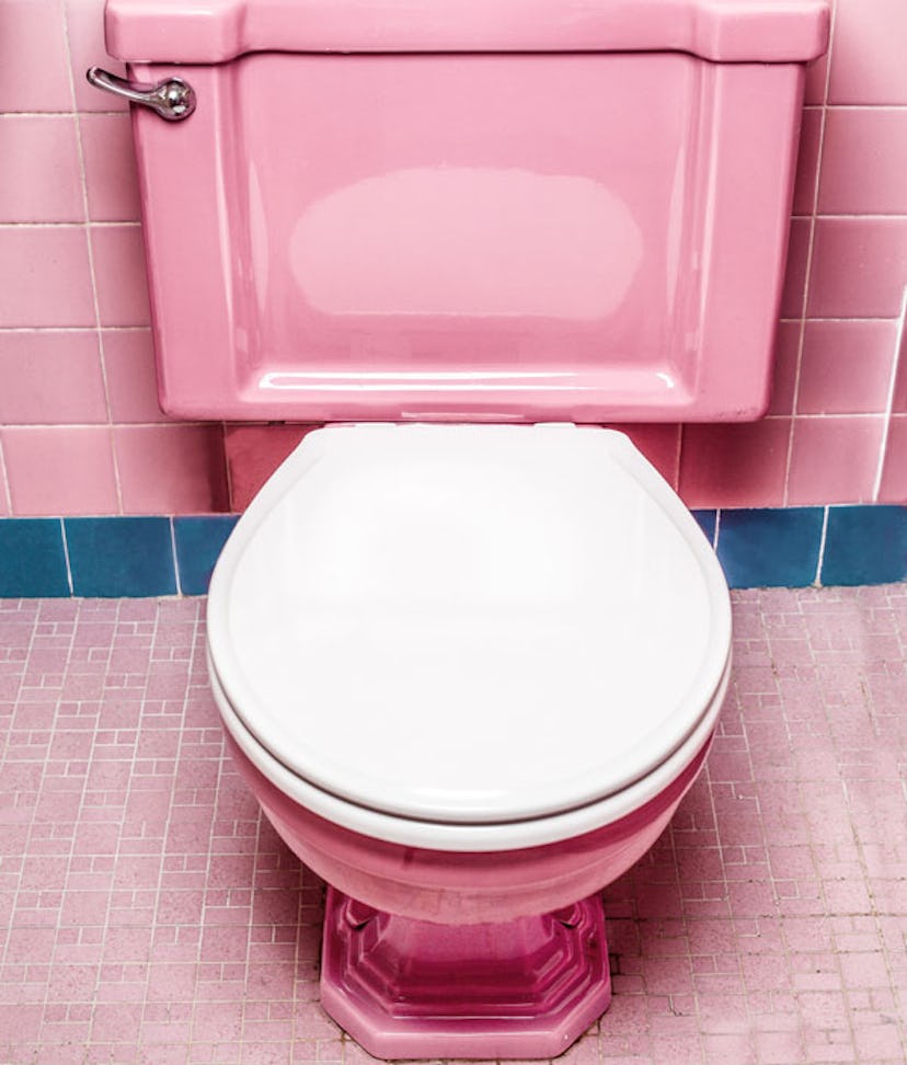 A  bathroom with pink tiles with blue details and a pink retro-style toilet seat