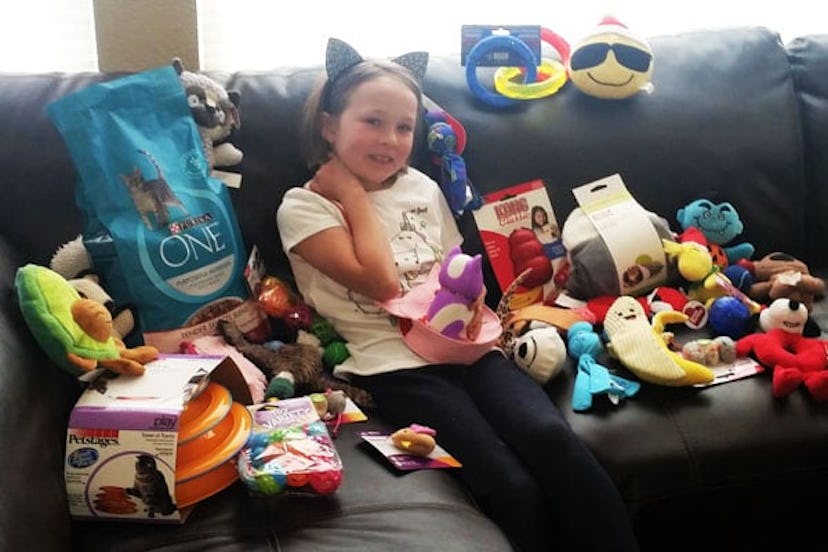 A little girl smiling and sitting on a couch surrounded by various toys