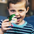 A boy with ADHD in a light blue and black T-shirt holding a dinosaur toy next to his mouth.