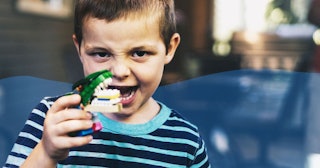 A boy with ADHD in a light blue and black T-shirt holding a dinosaur toy next to his mouth.