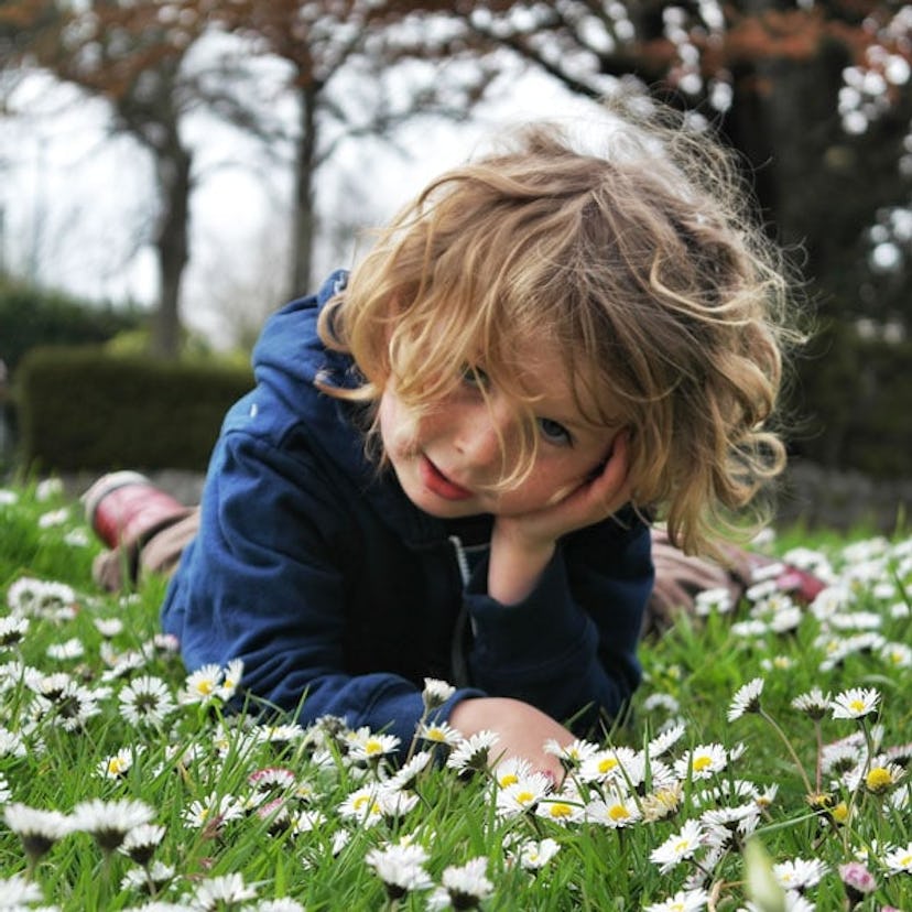 A blonde kid with ADHD lying in a field of daises.