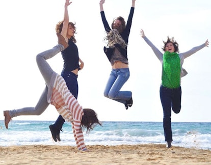 Four women smiling and jumping on a sand beach with the sea visible in the background