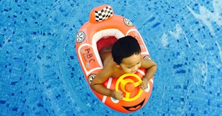 A boy sitting in an orange boat-like floatie in a swimming pool while smiling