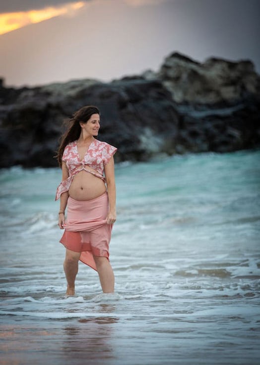 A pregnant lady standing in the sea and wearing a pink top and skirt