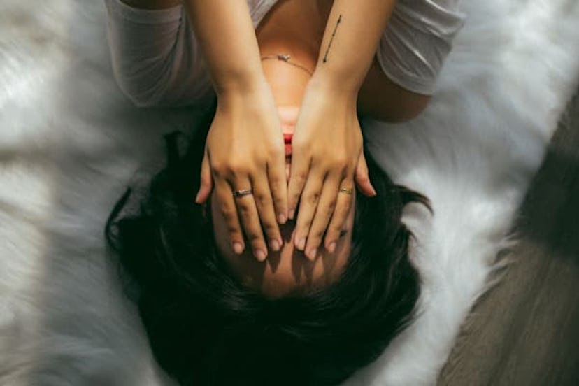 A  desperate woman laying on the bed covering her face with hands