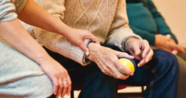 An old man in a brown sweater playing with a stretchy ball and a younger person sitting next to him ...