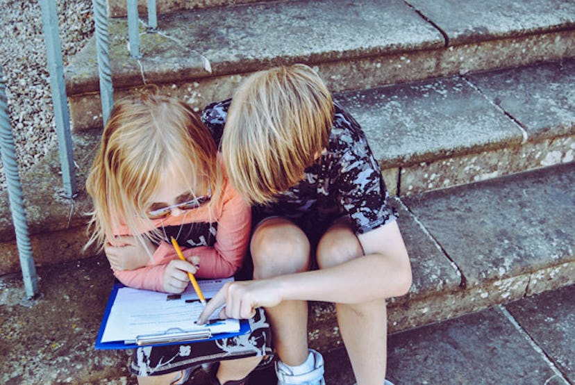 A brother helping his sister write her homework while sitting on outdoor steps as an act of kindness