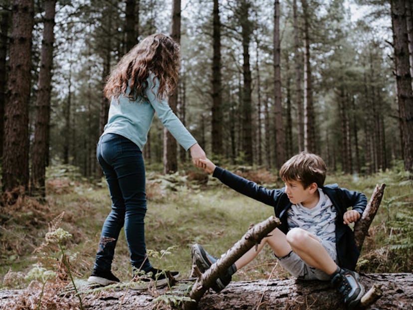 A young girl helping a young boy to get up in a forest as an act of kindness