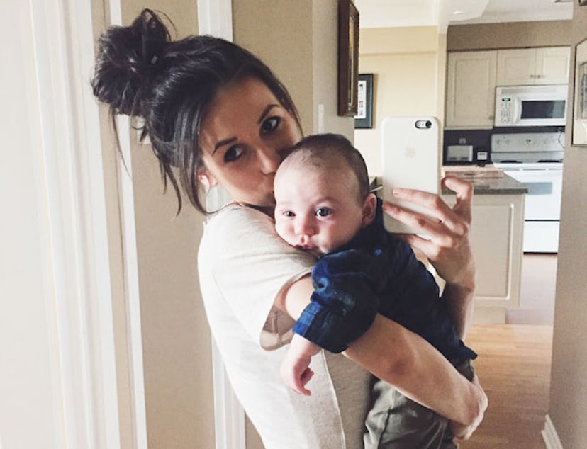 A dark-haired mother with her hair in a bun in a white T-shirt holding her baby in a blue shirt, tak...