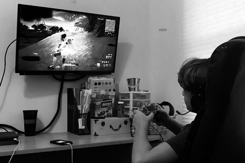 A boy playing Fortnite on his chair in his room with boxes and stationery on the desk