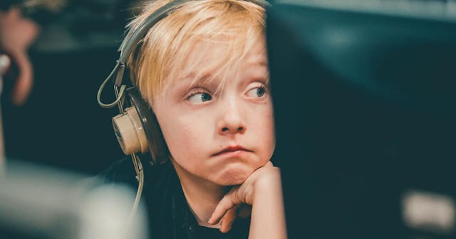 A blonde boy with bangs and his hand leaned against his chin, wearing large black-beige headphones