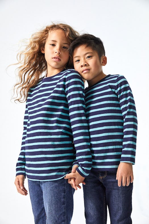 A girl and a boy holding hands in the same long-sleeved shirts in navy blue and blue stripes and blu...