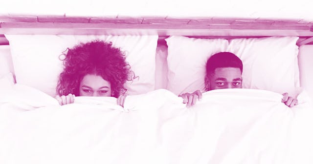 A couple lying in bed covering their faces with sheets