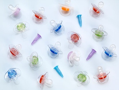 A number of different-colored pacifiers and IVF tubes spread out on a white background